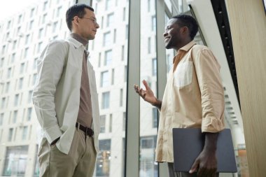 İşteki pencerede duran iki şık genç adamın düşük açılı portresi.