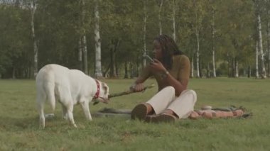 Tatlı beyaz labrador Retriever ve onun siyah bayan sahibi şehir parkında yeşil çimlerde dinlenirken birlikte oynuyorlar.