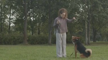 Kafkasyalı genç bir kadının, melez köpeğini parkta yeşil çimlerde eğitirken, ona pençe atmayı öğretirken.