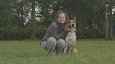 Kafkasyalı genç bir kadının portresi melez köpeğiyle parktaki yeşil çimlerde kameraya poz veriyor.