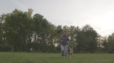 Beyaz kadın ve melez köpeğinin yaz tatilinin tadını çıkararak yeşil çimlerde birlikte koşması.