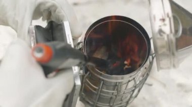 Arı çiftliğinde paslanmaz çelik içicide kurutucu odun yakarken eldiven takan tanınmayan arıcılara yakın çekim.