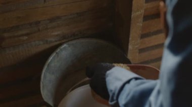 Kürek kaşığıyla metal kovaya giren çiftlik hayvanları için yulaf döken tanınmayan çiftçinin omzunun üstünden.