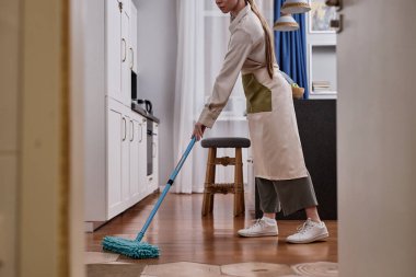 Hafta sonları yerleri paspaslayan ve daireleri temizleyen genç bir kadının yan görüntüsü.