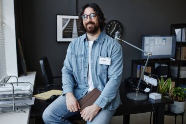 Tabletli genç sakallı adamın portresi ofisinde oturmuş kameraya gülümsüyor.