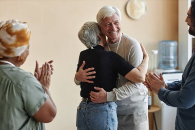 Neşeli bir grup yaşlı insan iyileşmeyi kutlayan destek grubunu alkışlıyor ve kucaklıyor.