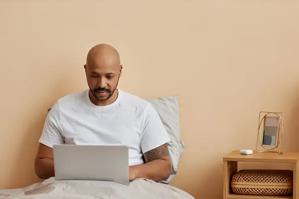 Minimal portrait of adult black man using laptop in bed in morning, copy space