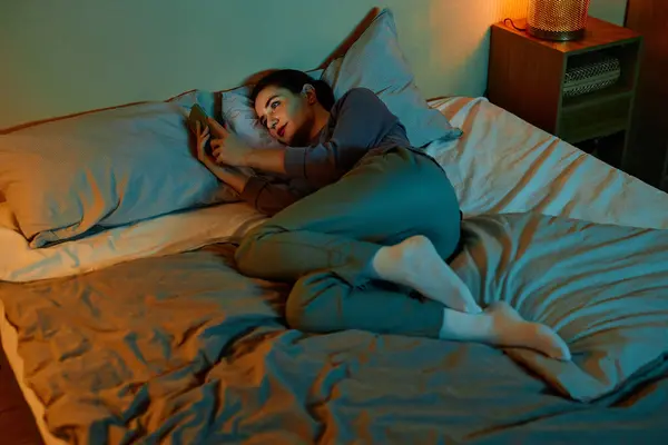 Full length portrait of lonely adult woman using smartphone in bed at night and scrolling social media, copy space