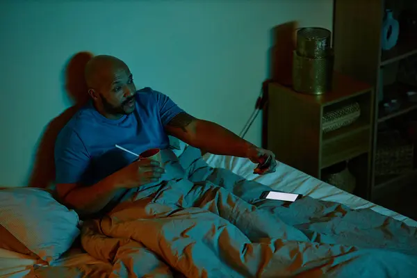 Portrait of black adult man watching TV in bed at night staying up late