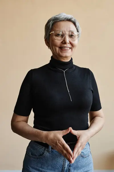 Waist up portrait of modern Asian senior woman looking at camera confidently