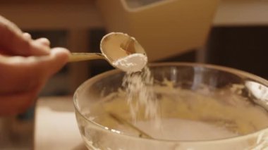 Evde yemek pişirirken cam kaseye un ve hamur karışımı katan tanınmamış bir kadının yakınlaşması.