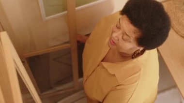 Yüksek açılı fotoğraf, sarı tişörtlü siyah bir kadın kitaplıktan kitap alıyor, evde boş zamanlarında okumaya karar veriyor.