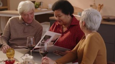 Üç eski çok ırklı arkadaşın fotoğraf albümündeki fotoğraflara baktığı ve rahat bir dairede birlikte yemek yerken hayatı andığı orta boy bir fotoğraf.