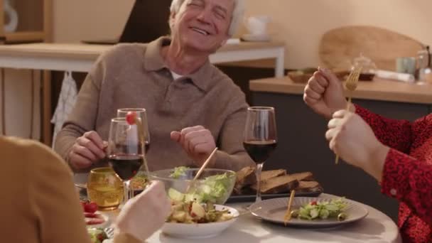 家庭で一緒に夕食を楽しむ3人の民族的に多様な高齢者の友人の中型ショット 楽しいチャットとワイングラスで試飲 — ストック動画