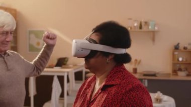 Yaşlı siyahi kadın ve arkadaşlarının evde VR oyunu oynamalarının orta yavaşlığı. Birlikte eğleniyorlar.