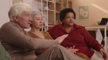 Üç farklı etnik kökene sahip arkadaşın televizyon karşısında rahat bir dairede oturup maç izlediği orta boy bir fotoğraf.