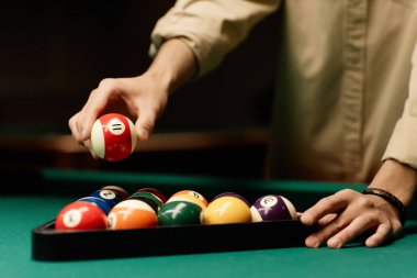 Kırmızı bilardo topunu düşük ışıklı fotokopi masasının üzerinde tutan erkek elini kapat.