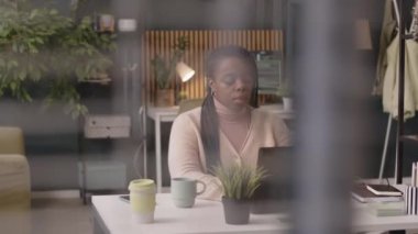 Modern ve yeşil ofiste çalışan, dizüstü bilgisayarın önünde oturan genç siyahi kadın çalışanın belini kaldırın.