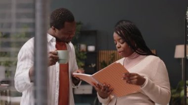 Genç Afrikalı Amerikalı iş arkadaşlarının proje fikirleriyle deftere baktığı ve modern yeşil ofis alanında tartışırken orta boy bir fotoğraf.