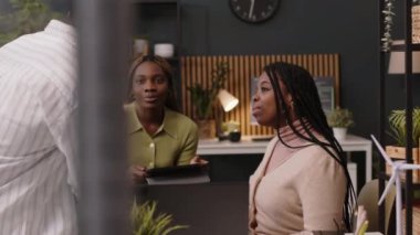 Yeşil ofiste işbirliği yapan, fikir alışverişi yapan ve sohbet eden üç kişilik genç ve yaratıcı Siyah girişimci ekibinin orta boy fotoğrafı.