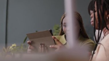 Bir grup genç siyahi erkek ve bayan meslektaşın tablete bakması ve yeşil ofiste çalışırken yaratıcı proje farkındalığı üzerine iletişim kurmaları.