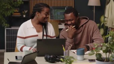 Orta halli, genç, Afro-Amerikan yaratıcı iş arkadaşlarının modern sürdürülebilir ve çevre dostu yeşil ofislerinde dizüstü bilgisayar ve iletişim kurarak oturduğu bir fotoğraf.