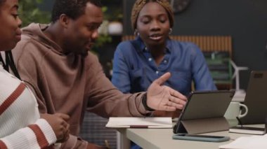 Modern ortak çalışma alanında birçok ev bitkisiyle yapılan beyin fırtınası sırasında dijital tablete bakıp işaret eden genç Afro-Amerikan ofis ekibinin belini kaldırın.
