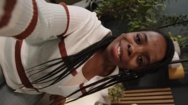 Çağdaş yeşil ofis alanında bir gün boyunca video kaydederken kameraya konuşan gülümseyen Afrikalı Amerikalı genç kadının el kamerası görüntüsü.