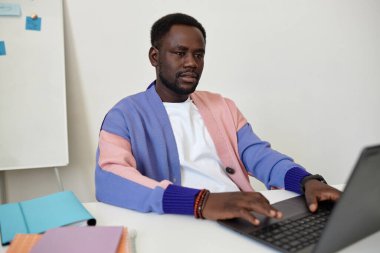 Ofiste dizüstü bilgisayar kullanan ve renkli kıyafetler giyen yaratıcı siyahi adamın portresi.