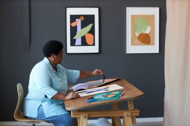 Üst düzey kadın tasarımcının günlük kıyafetleri içinde yan görünüşü kompozisyona bir parça kağıt eklerken yeni bir uygulama yaratıyor