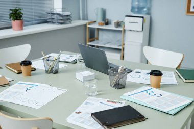 Çeşitli ofis malzemeleri, dizüstü bilgisayarlar, not defterleri, kahve fincanları, kalemler ve kalemler, bir bardak su ve grafik verili finansal kağıtlar.
