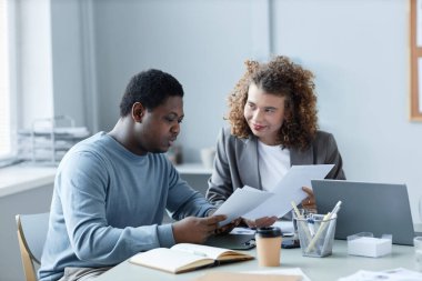 Genç Afrikalı Amerikalı erkek simsar ve bayan meslektaşı toplantıda belgeleri tutarken mali verileri tartışıyorlar.