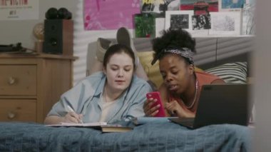 20 'li yaşlarının başındaki iki farklı kızın göğüsleri rahat yurt odasında dizüstü bilgisayarla yatıp üniversiteye hazırlanıyor.