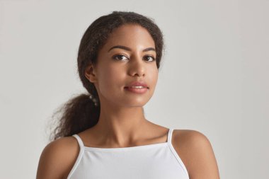 Beyaz, basit güzelliğe karşı kameraya bakan genç Afrikalı Amerikalı kadının yakın plan portresi.