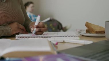 Tanımlanamayan Afro-Amerikan üniversite öğrencisi beyaz bir kadın oda arkadaşıyla arka planda bulanık bir şekilde otururken, çalışırken not defterine notlar yazarken çekilmiş görüntüler.