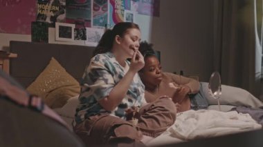 İki farklı genç kız arkadaş sohbet ediyor ve yatıya kalma sırasında rahat bir yatak odasında makyaj yapıyorlar.