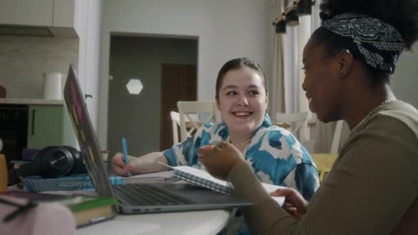 2名年轻的多民族女大学生白天一起在现代公寓的桌旁用笔记本电脑聊天 — 图库视频影像