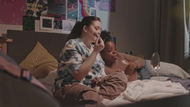 Две Молодые Разноплановые Подружки Общаются Делают Макияж Кровати Уютной Спальне — стоковое видео