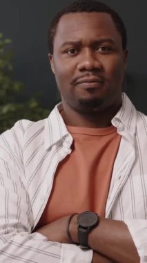 Dikey Belden yukarı, gülümseyen genç bir zencinin modern yeşil ofiste elleri katlanmış, kameraya poz veren portresi.