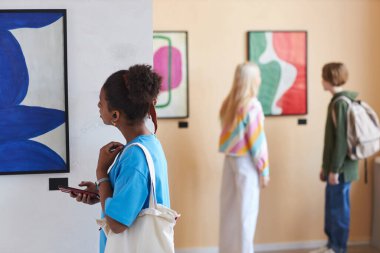 Modern sanat galerisi ya da müzesinde sanat eserlerine bakan çeşitli gençlerin renkli bir fotoğrafı.