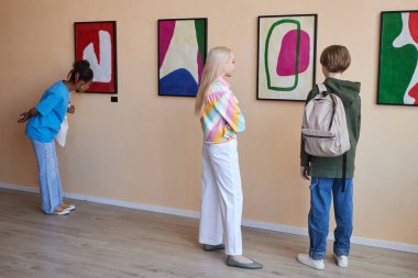Sanat galerisinde ya da müzede sergilenen soyut sanat eserlerine bakan çeşitli gençlerden oluşan bir grup.