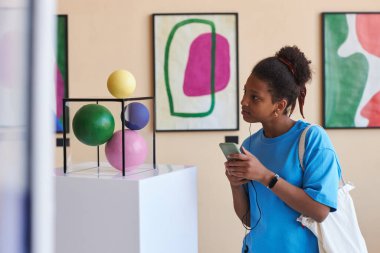 Modern sanat galerisindeki heykele bakan Afrikalı Amerikalı genç kızın renkli portresi