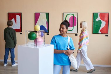 Müzede soyut sanat eserlerine bakan bir grup gencin renkli portresi.