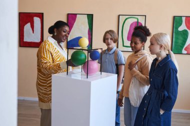 Modern sanat galerisi veya müzesinde öğretmenlik ya da tur rehberliği dinleyen çeşitli gençler.