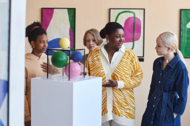 Modern sanat galerisinde öğretmen ya da tur rehberini dinleyen çeşitli gençler.