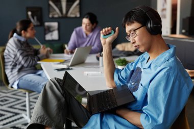 İş yerinde el açıcı kopyalayıcı ile otururken bilgisayarın ekranına bakan Asyalı genç adamın yan görünüm portresi