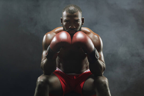 Dramatic front view portrait of muscular African American boxer looking at camera intensely with smoke in background