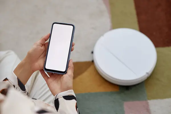 家のコピースペースでロボット掃除機を操作しながら 白い画面でスマートフォンを保持している認識できない女性のトップビュークローズアップ — ストック写真