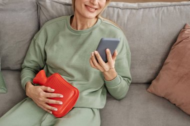Gülümseyen kadının karnına kırmızı sıcak su şişesi dayayıp fotokopi makinesinde akıllı telefon kullanmasına yakın durun.