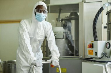 İlaç fabrikasında çalışan maskeli ve koruyucu giysili siyah bir adamın portresi.